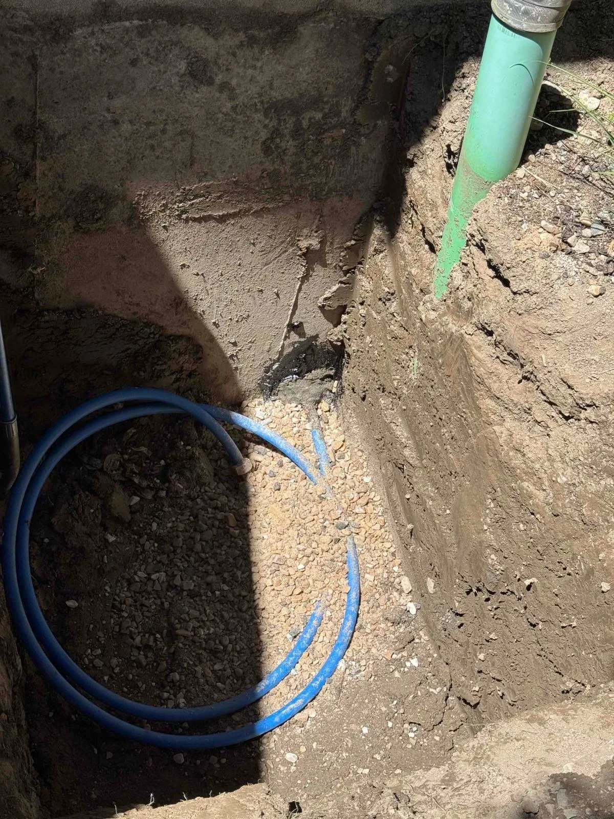 Blue water service line and green sewer pipe exposed in a trench in Utah