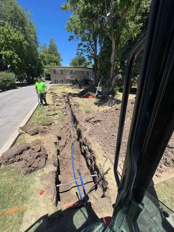 Water service line trench along a Utah street seen from an excavator cab