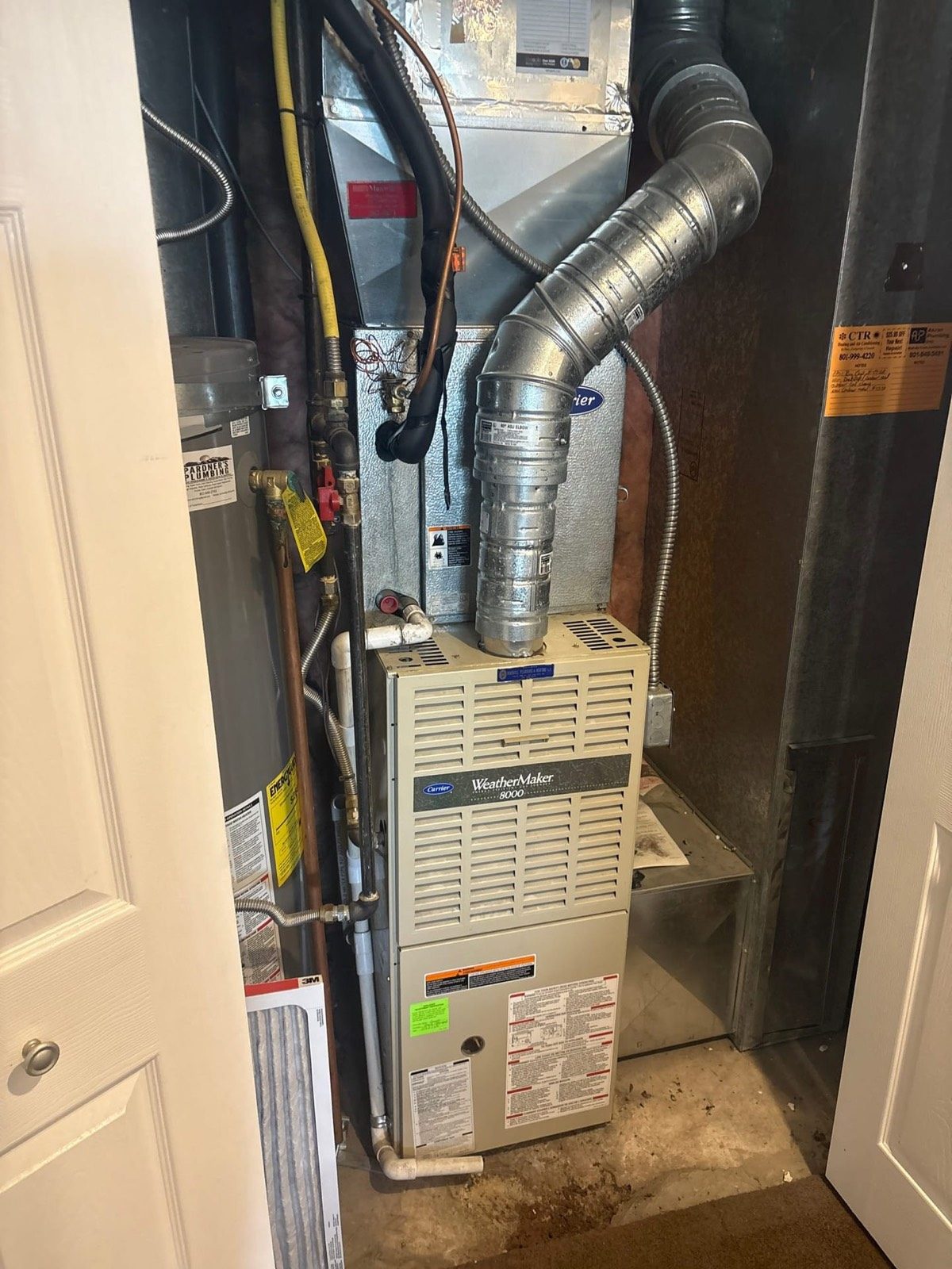 Gas furnace and water heater in a closet with third party contractor service tags on the wall