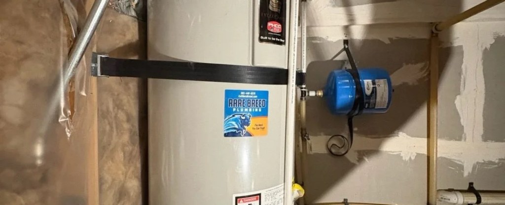 Water heater with a Rare Breed Plumbing service sticker and expansion tank in Utah