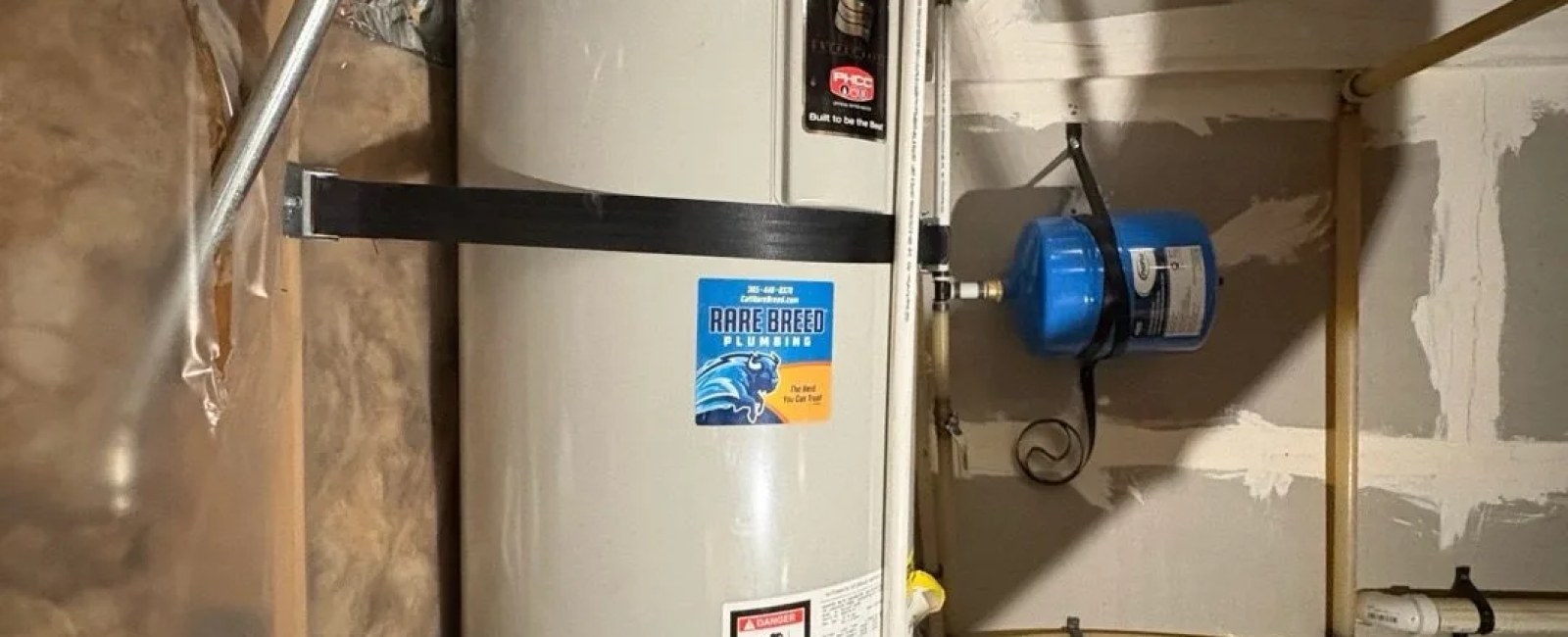 Water heater with a Rare Breed Plumbing service sticker and expansion tank in Utah