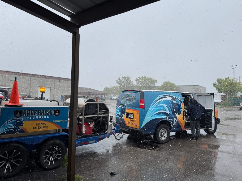 Rare Breed Plumbing hydro jetter trailer hitched to a service van while a technician loads out at the shop