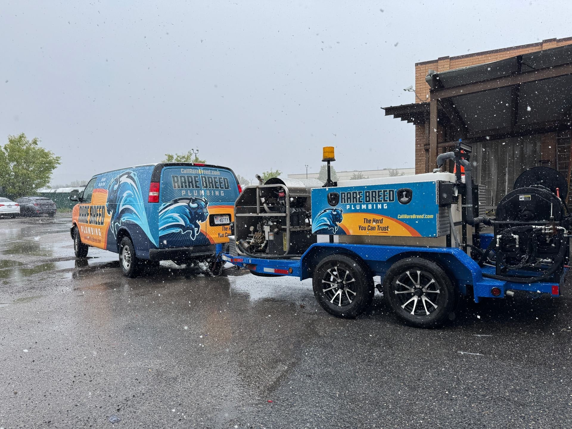 Rare Breed Plumbing van and the hydro jetter trailer staged outside the shop in a spring storm